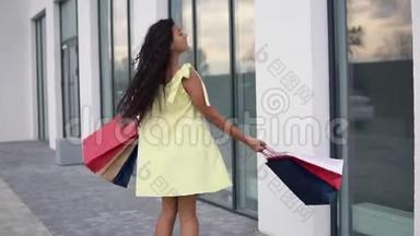 漂亮的女孩模特穿着一件长裙，购物后手里拿着彩色袋子，心情很好。 慢动作。 高清高清